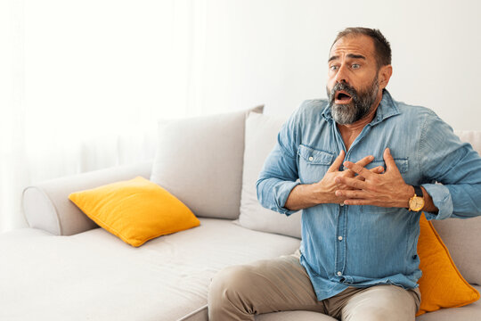 Shocked Mature Man Sitting on Sofa with Hands on Chest