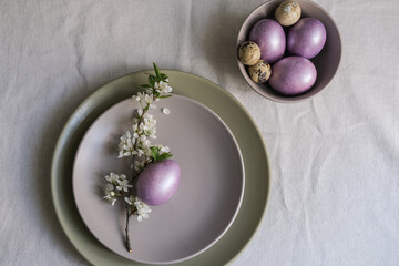 Top view of pastel purple Easter eggs on plate with blossom branch. Easter table setting idea