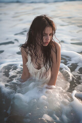 Obraz premium Young woman in a white dress sitting in the ocean waves at dusk, conveying introspection and calm