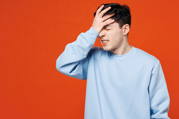 Young sad Caucasian man wears blue sweatshirt casual clothes put hand on face facepalm epic fail mistaken omg gesture isolated on plain red orange color background studio portrait. Lifestyle concept.