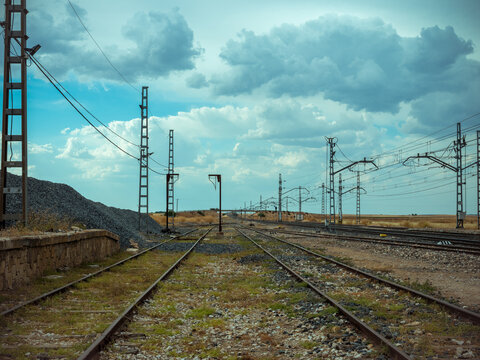 Railway tracks crossing rural landscape under cloudy sky