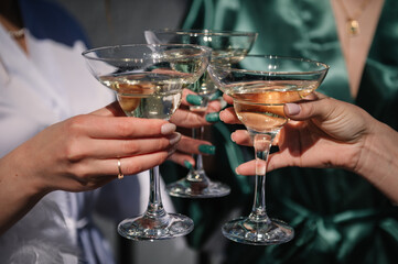 Cheers. Pretty young ladies friends wear silk robes hold glasses with champagne in hotel. Bride and bridesmaid celebrate bachelorette spa party. Closeup three female hands holding cocktails and drink.