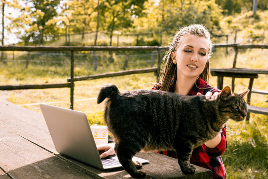 Woman petting cat while working on laptop outdoors