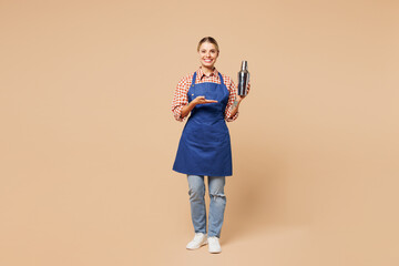 Full body young woman barista bartender barman employee wear blue apron shirt work in coffee shop hold shaker make alcohol cocktail isolated on plain beige background. Small business startup concept.