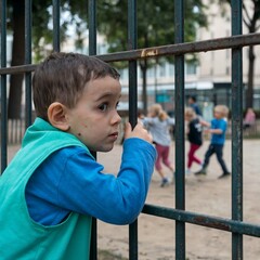 Young Boy Peeking Through the Bars of a Playground Fence