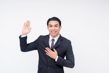 A young asian business executive swearing an oath and placing his hand in his chest, promising to be truthful. Isolated on a white background.