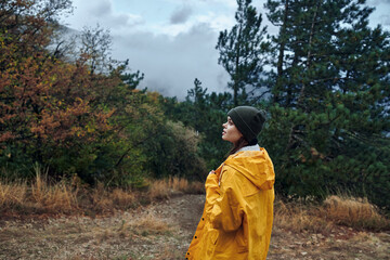 Lonely woman in a bright yellow raincoat standing on a forest road looking up at the sky in contemplation