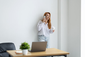 Businesswoman is enjoying a cup of coffee while talking on the phone in modern office