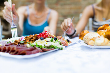 Friends enjoying a colorful spread of meats, salads, and bread at an outdoor gathering during a sunny day