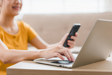 A woman in yellow shirt is using laptop while holding smartphone, showcasing modern workspace. scene reflects productivity and multitasking in cozy environment.