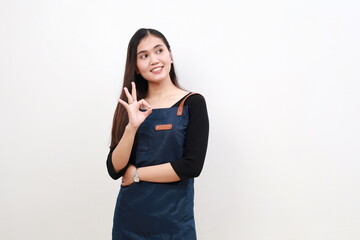 Portrait smiling young asian woman wearing apron showing okay sign gesture with hand, looking at empty space isolated white background, waitress or entrepreneur, small business or startup.