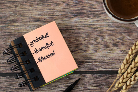 Grateful, thankful, blessed, handwritten text in notebook with coffee cup and wheat on wooden table. Top view. Biblical concept of Christian gratitude and thanksgiving to God Jesus Christ.