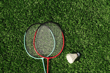 Two badminton rackets and white badminton shuttlecock on green lawn. Summer leisure games. Outdoors. View from above.