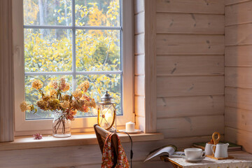 Autumn still life in a beautiful wooden house. A cup of hot tea, a teapot, honey, candles and books on the table. Golden autumn outside the window, leaf fall