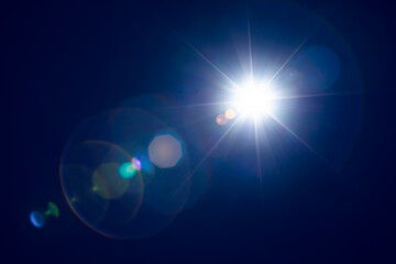 Bright sunlight shining in dark blue sky with lens flares.