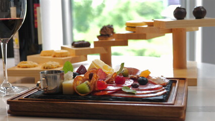 Culinary display featuring variety of gourmet appetizers and desserts on stylish serving board, accompanied by glass of red wine, presented in upscale dining setting. Fine Dining and Gourmet Food.