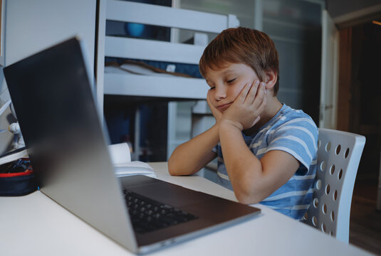 cute little boy studying at home using laptop, tired, sressed, thinking hard trying to do homework