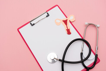 Stethoscope and medical clipboard with uterus cutout on pink background, representing women's health