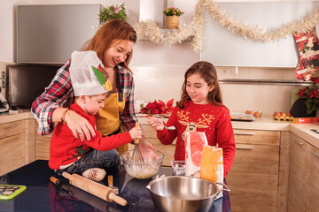 Single mother making cookies with her children in the kitchen on Christmas Day. Concept: together
