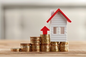 Red graph chart rising up on stack coins and house model on wooden table white wall background
