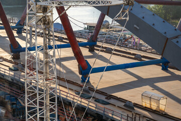 The construction of a bridge is underway with a white crane standing tall in the center of the image, supporting the steel beams overhead