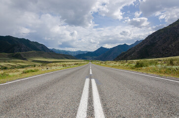 Driving down an empty road with a view of mountains in the distance and cloudy sky through. Road line center