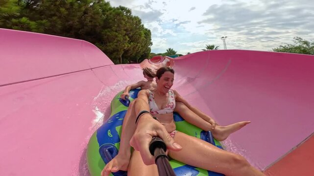 Selfie of woman and teenager sliding a water slide very fast on a rubber ring. Son and mother having fun, going down a water slide at a Water Amusement Park on summer vacation. 4k video.
