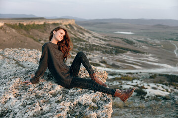 Serene woman sitting on rocky ledge with panoramic view of valley and mountains in background