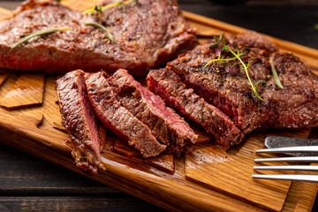 Grilled beef steak, well done with seasons and green on a black wooden background close up