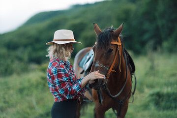 Obraz premium Happy blonde with horse in forest. Woman and a horse walking through the field during the day. Dressed in a plaid shirt and black leggings.