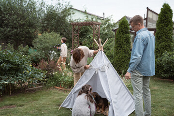 Parents set up a teepee house in the garden for plays of their kids and dog © Natalia Navodnaia
