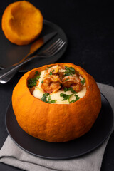 Whole baked pumpkin with tiger prawns, melted cheese and tomatoes. Traditional dish of Brazil, home cooking. Selective focus, close-up, black background.