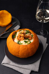 Whole baked pumpkin with tiger prawns, melted cheese, tomatoes and a glass of white wine. Traditional dish of Brazil, home cooking. Selective focus, close-up, black background.