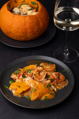 Whole baked pumpkin with tiger prawns, melted cheese, tomatoes and a glass of white wine. Traditional dish of Brazil, home cooking. Selective focus, close-up, black background.