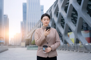Fototapeta premium Stylish Urban Professional Woman Engaged with Smartphone in Cityscape
