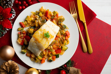 Cod with baked vegetables traditional Spanish recipe. Food on table with Christmas decorations.