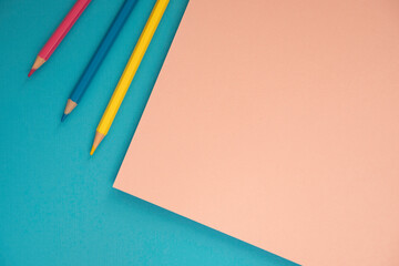 Education, back to school, craft art project concept. Light blue, pink and yellow pencils lying on colorful geometric paper background. Top view, flat lay
