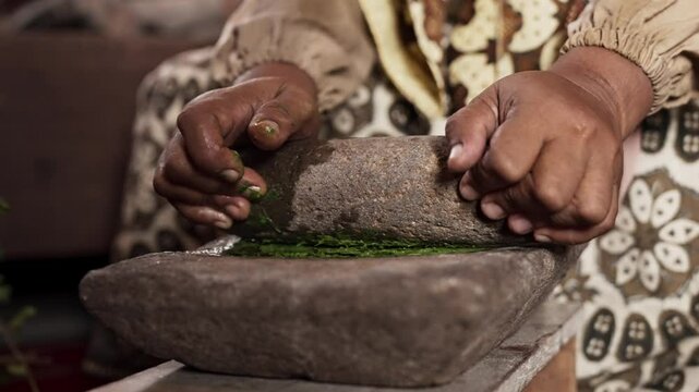 An Asian woman grinds leaves from the henna tree to make henna paste