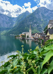 A picturesque view of the lakeside village of Hallstatt, Austria, with its iconic church and dramatic alpine mountains reflected in the clear waters of Lake Hallstatt.