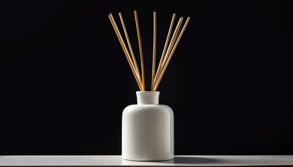 White ceramic diffuser bottle with natural wood reeds, isolated on black background.
