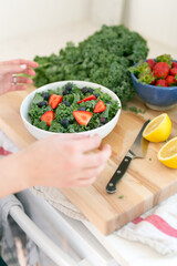 close up of hands making salad with strawberries on butcher block cutting board styled with ingredients