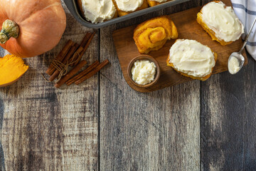 Freshly baked pumpkin cinnamon rolls or cinnabon with cream cheese on a rustic wooden table. Homemade seasonal autumn homemade pastry.