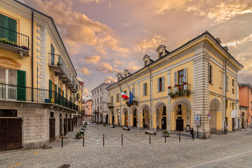 Obraz premium Caraglio, Piedmont, Italy - September 06, 2024: The Town Hall building with arcades in coblestone Giolitti Square with sunset sky