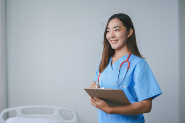 Young female doctor smiling and taking notes on clipboard in hospital room