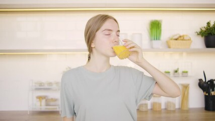 A young woman is enjoying a refreshing glass of fresh juice while standing in a stylish modern kitchen, embracing the joyful moment