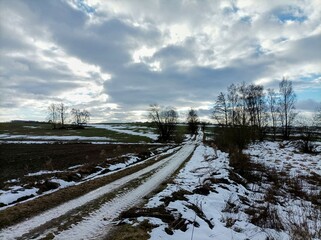 Snowy countryside in the Czech republic. Snow on a field. Cloudy sky and freezing weather. Country road with trees in winter. European Christmas.