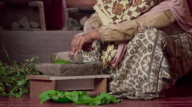 An Asian woman grinds leaves from the henna tree to make henna paste