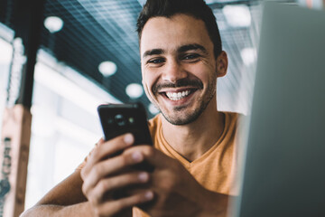 Portrait of happy hipster blogger with modern mobile phone in hands smiling at camera while...