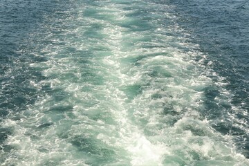 Boat waves formed while sailing on sea. Wake of vessel. Wide wake trail from boat. Back view. Ocean water. Trace from large ship. Ship cuts through foamy white waves of deep blue sea. White Bubble