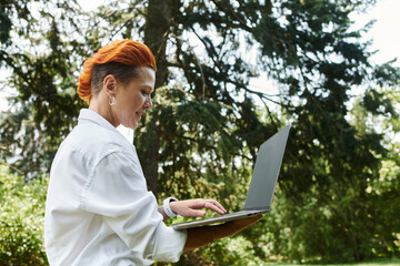 A teacher with bright red hair uses her laptop outdoors.
